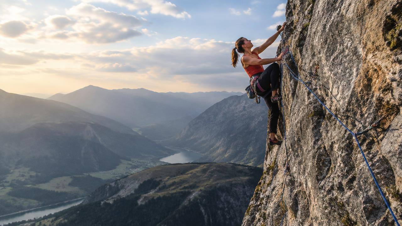 Rock climber secured by rope on a cliff above a valley